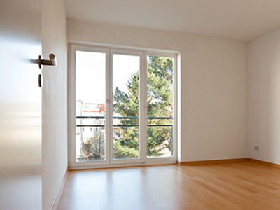 Ein leerer Raum mit großen Fenstern und Parkettboden.